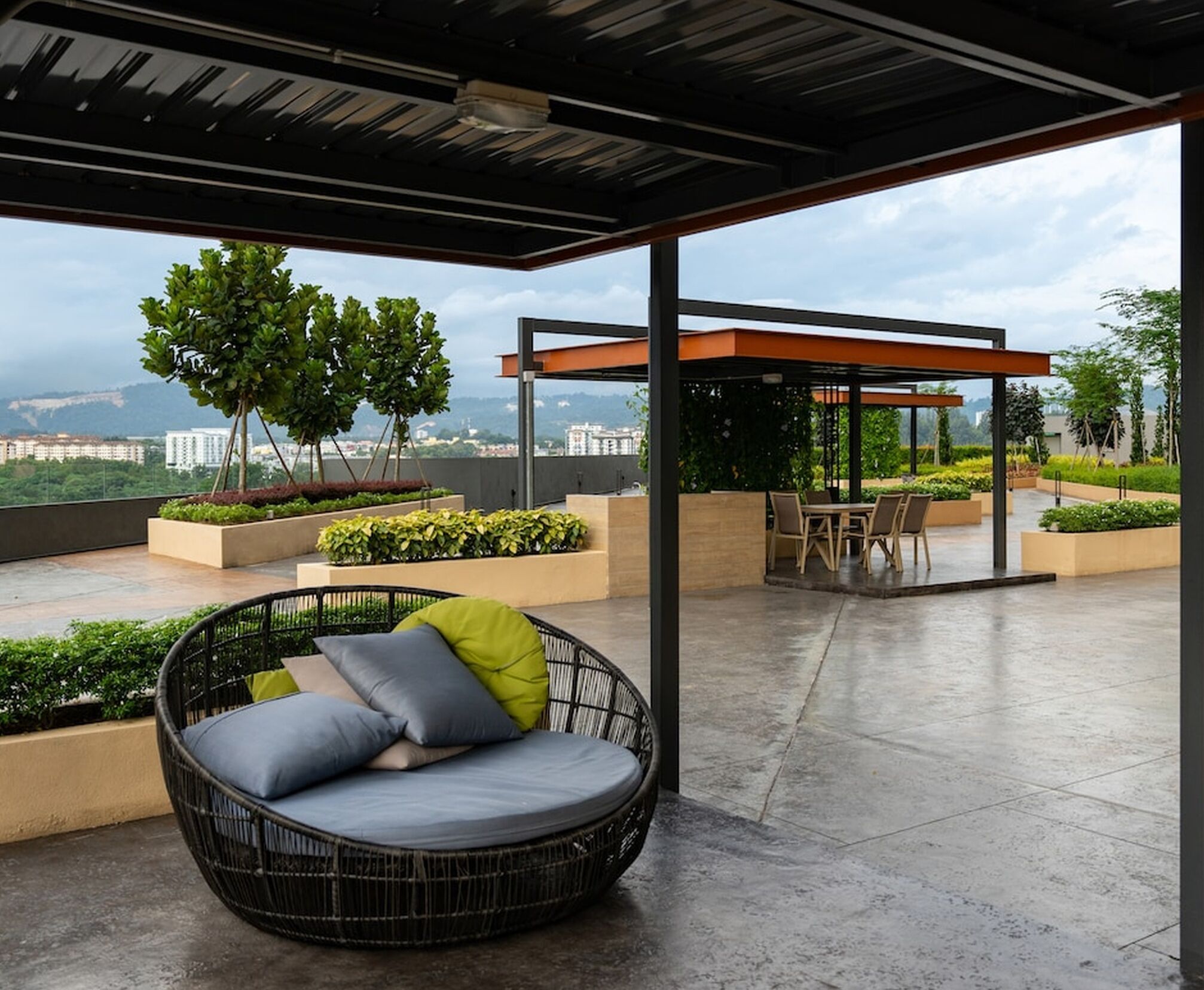 Un espace extérieur aménagé, abrité et doté de sièges, avec une chaise en osier et une table, entouré de jardinières et offrant une vue sur le paysage urbain.
