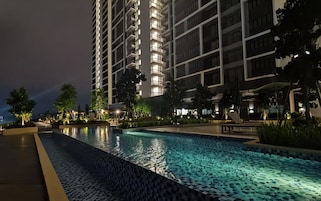 A nighttime view of a modern hotel with a swimming pool, surrounded by well-lit buildings and landscaped areas.
