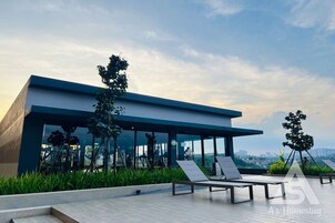 A modern building with large windows, a rooftop terrace with lounge chairs, and a view of the cityscape.