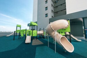Un parque infantil con toboganes y estructuras para escalar, situado en una azotea con vistas a la ciudad.