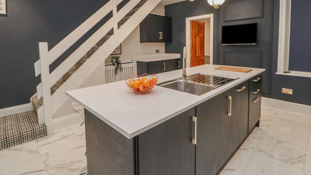 Una cucina moderna con mobili scuri, un piano di lavoro bianco e un'isola centrale con una ciotola di frutta.