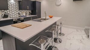 Una cucina moderna con isola centrale, sgabelli da bar, forno integrato e una decorativa parete di fondo.
