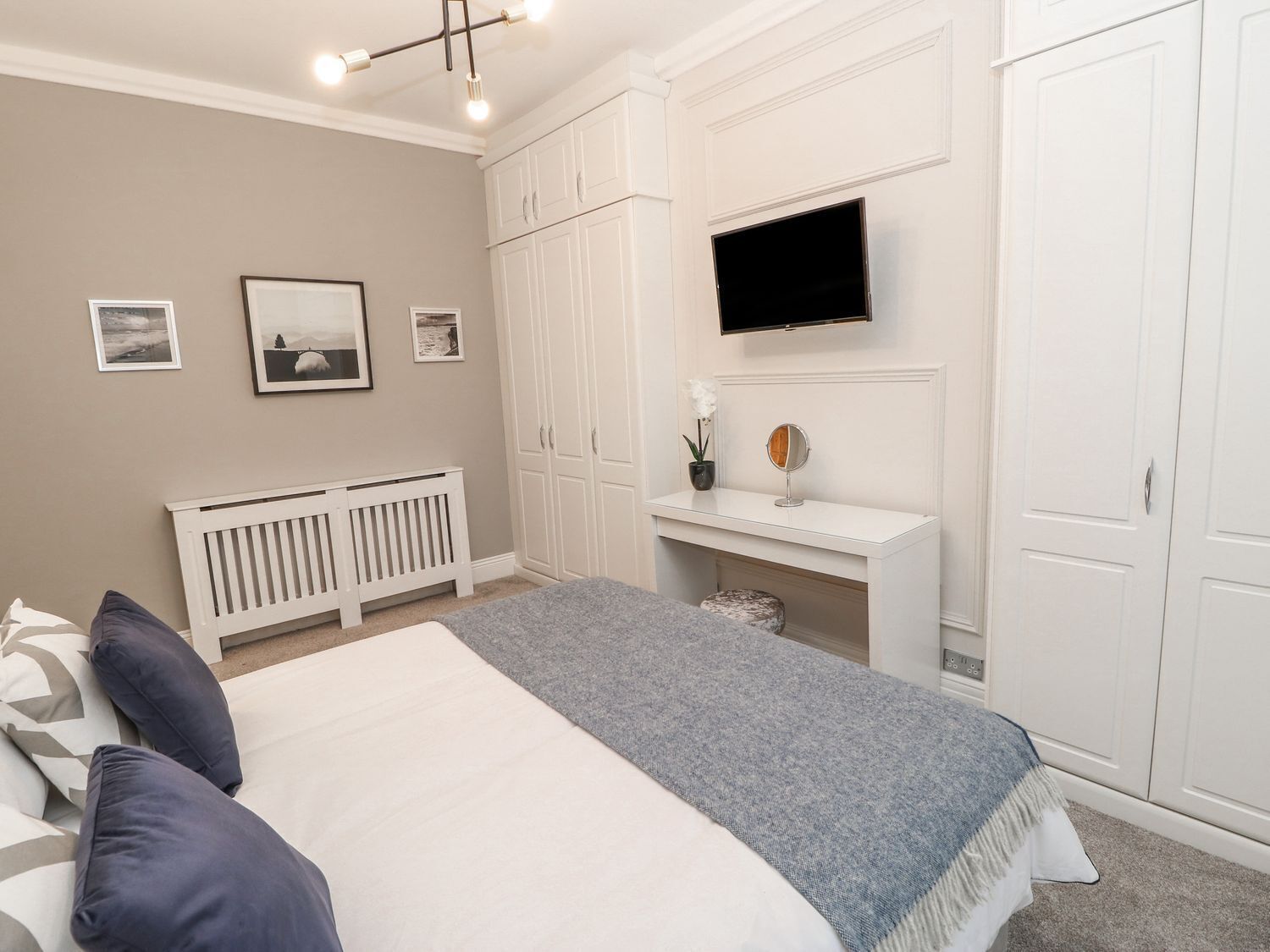 A bedroom with a bed, a white wardrobe, a TV mounted on the wall, and a radiator.