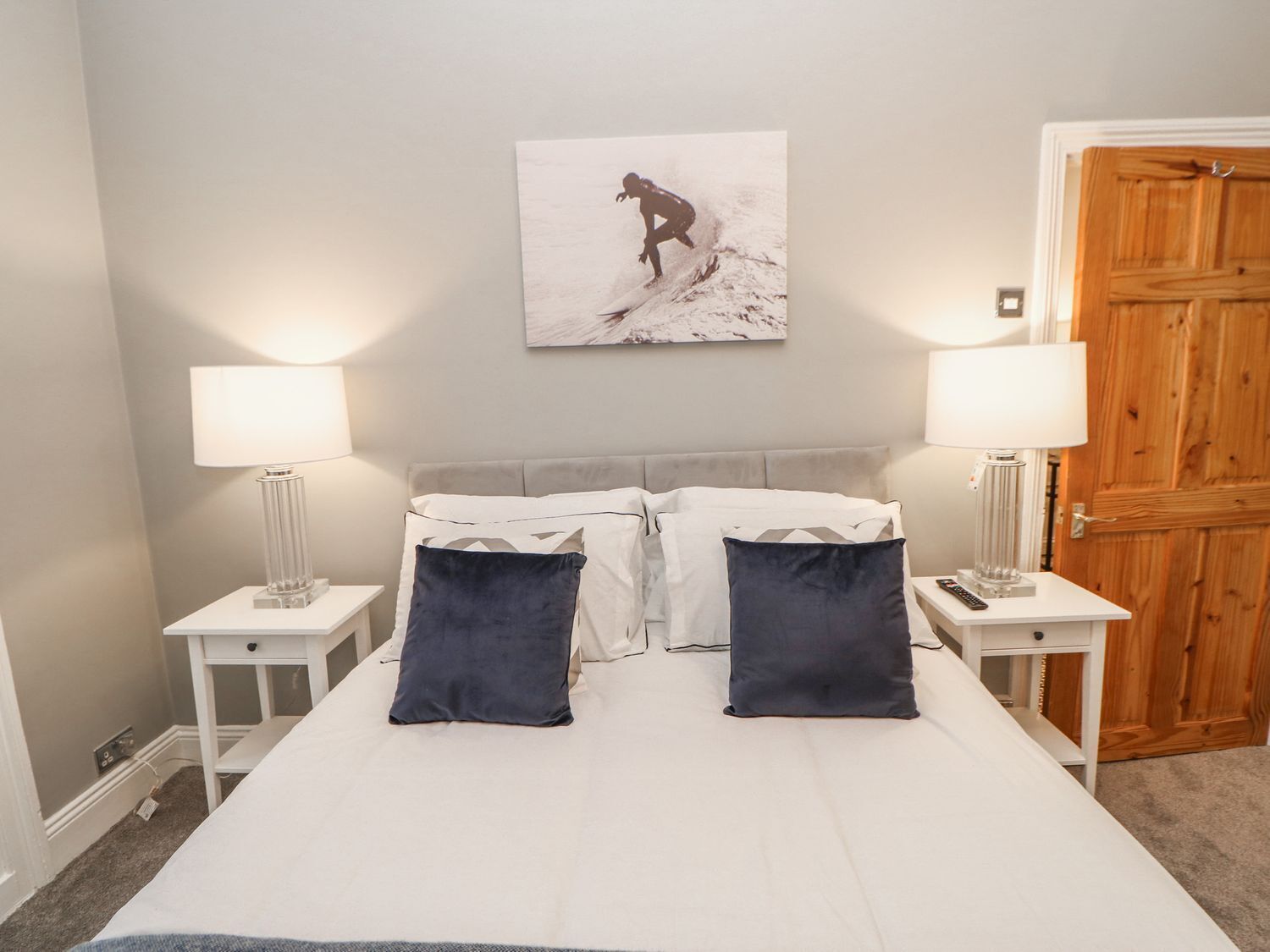 Une chambre à coucher comprenant un lit, deux tables de chevet, deux lampes, une porte en bois et un tableau accroché au mur.