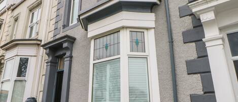 A corner bay window with white shutters, a black door, and a white picket fence.