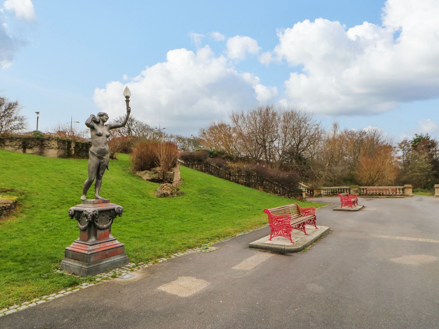 A statue on a pedestal in a park with benches and a paved path.