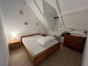 Un dormitorio con techo inclinado, una cama de madera, una mesita de noche con lámpara y un aparador.