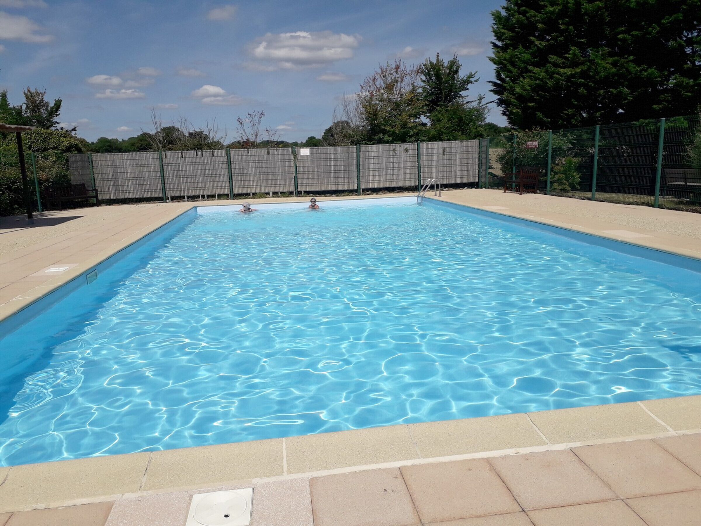 Ein rechteckiger Swimmingpool mit klarem, blauem Wasser, umgeben von einer gefliesten Liegefläche und einem Metallzaun.