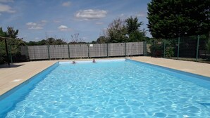 Ein rechteckiger Swimmingpool mit klarem, blauem Wasser, umgeben von einer gefliesten Liegefläche und einem Metallzaun.
