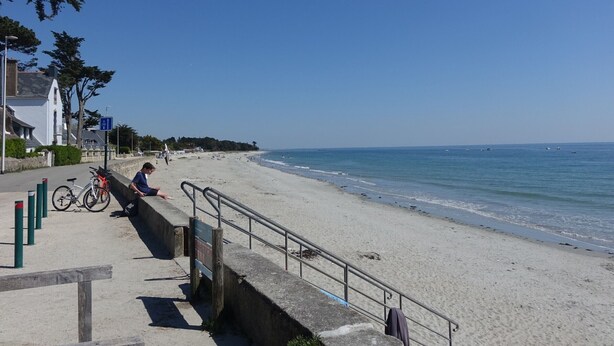 Ein Strand mit einer Betonpromenade, Fahrrädern und blauem Himmel.