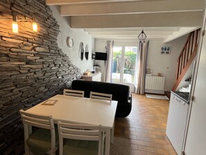 A dining area with a stone wall, a white table, and chairs. There is a black sofa and a television mounted on the wall. - House 300m from the beach with parking (Sarzeau)