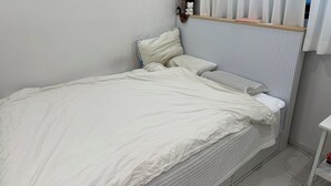 A single bed with white bedding, a bedside table with a lamp, and a window with vertical blinds. - Sweet Stay Seoul (Seoul)