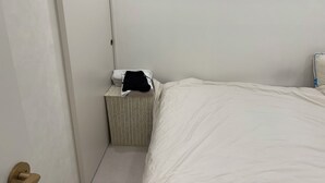 A small, clean room with a bed, a bedside table, and a basket. - Sweet Stay Seoul (Seoul)