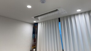 A modern hotel room with a white ceiling, recessed lighting, a ceiling-mounted air conditioning unit, and a large window with white curtains. - Sweet Stay Seoul (Seoul)