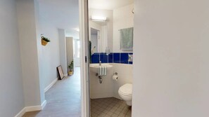 Un pasillo estrecho que lleva a un baño con un lavamanos blanco, azulejos azules y un inodoro.