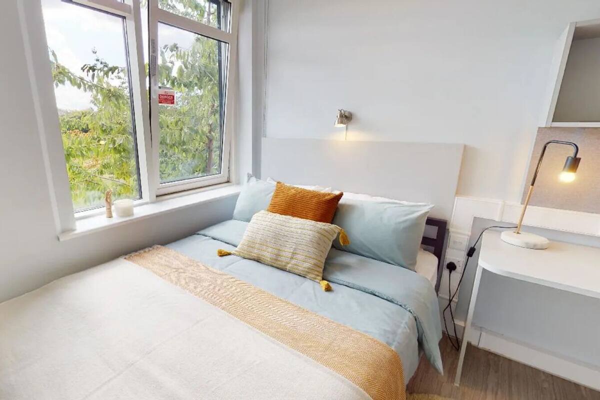 Une chambre à coucher comprenant un lit, une table de chevet, une lampe et une fenêtre donnant sur un paysage verdoyant.