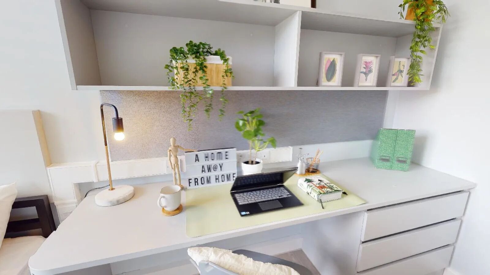 A modern workspace with a desk, laptop, and a sign reading "A HOME AWAY FROM HOME".