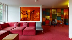Un salon moderne avec un canapé rouge, une table basse en bois et un tableau abstrait aux couleurs vives accroché au mur.