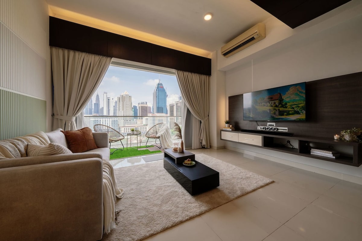A modern living room with a sofa, coffee table, and TV. A large window offers a city view.