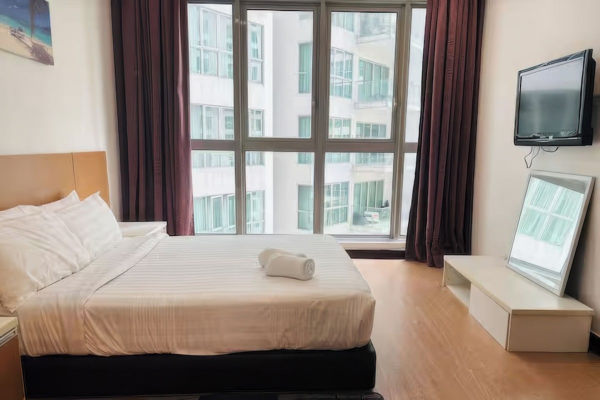 A hotel room with a large bed, a flat-screen TV, a window with curtains, and a painting on the wall.