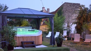 Una vasca idromassaggio sotto un gazebo in un giardino privato, con un muro in pietra e poltrone relax.