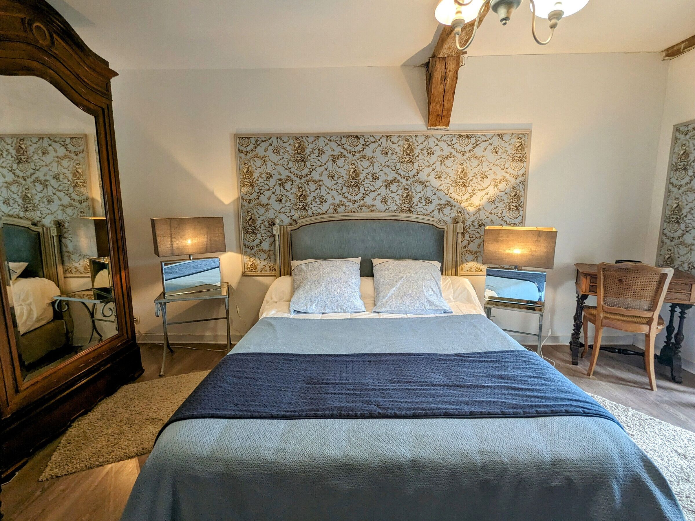 Une chambre à coucher avec un grand lit, deux tables de chevet, une chaise, un miroir et un lustre.