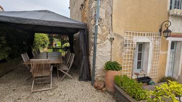 Eine Terrasse im Freien mit Holztisch und -stühlen, einem überdachten Bereich und Pflanzkübeln.