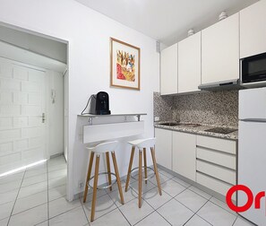 Una cocina moderna con gabinetes blancos, microondas, cafetera y dos taburetes.