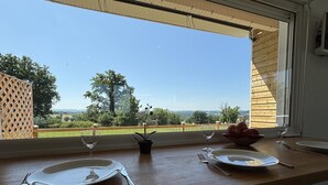 Een eettafel gedekt met borden, bestek en een fruitschaal, met uitzicht op een groen landschap door een raam.