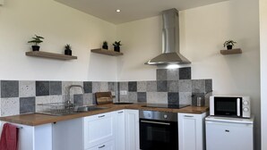 Een moderne keuken met witte kasten, een roestvrijstalen afzuigkap, een inbouwoven, een magnetron en een betegelde spatwand.