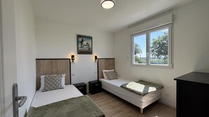 Een slaapkamer met twee bedden, een raam, een schilderij en een plafondlamp.