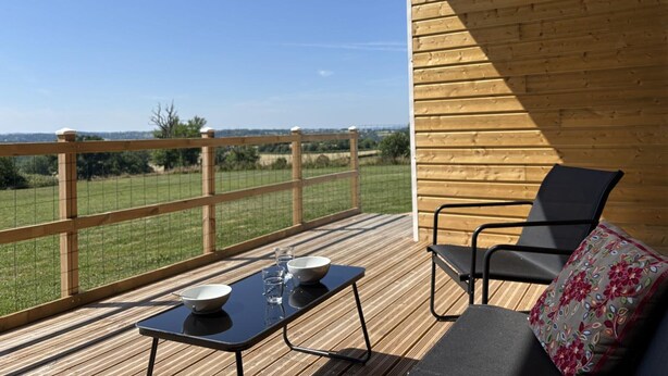 Een houten terras met een tafel en stoelen, met uitzicht op een groen landschap.