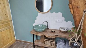 Een badkamer met een houten wastafel, een ronde spiegel, een groene keramieken wasbak en een hangende plant.