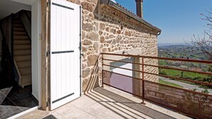 A stone building with a white door, a staircase leading to a balcony, and a view of the countryside. - Spacious and modern cottage with terrace in the heart of nature (Saint-Appolinard)