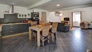 A modern kitchen with dark cabinets, a dining table with wicker chairs, a grey sofa, and a TV in the living area. - Spacious and modern cottage with terrace in the heart of nature (Saint-Appolinard)