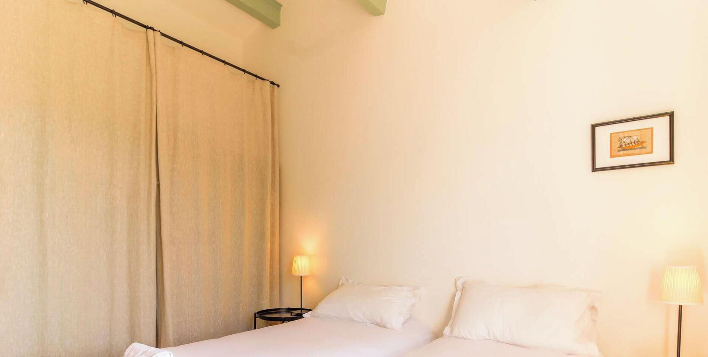 Una habitación de hotel con una cama, una mesita de noche, una lámpara, una cortina y un cuadro en la pared.