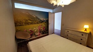 Un dormitorio con cama, una silla, un aparador y un mural de un paisaje montañoso.