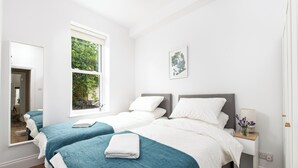 Een hotelkamer met twee bedden, een groot raam, een nachtkastje met een lamp en een lijst aan de muur.