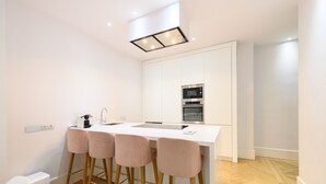 A modern kitchen with a white countertop, stainless steel appliances, and pink bar stools.