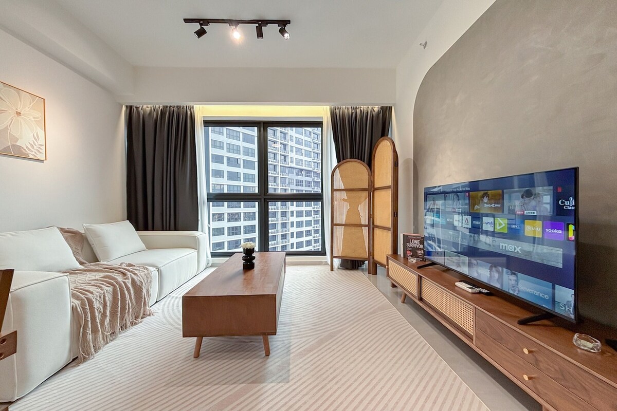 Een moderne woonkamer met een witte bank, een houten salontafel, een flatscreen televisie en een groot raam met gordijnen.