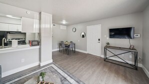 A modern kitchen with white cabinets, a built-in microwave, and a stainless steel refrigerator. There is a dining area with a table and chairs, and a TV mounted on the wall. - Beautiful 1Bd/1Bd Apartment in Dallas (Dallas)