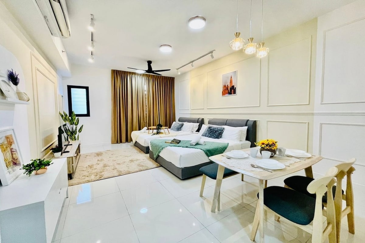 A modern hotel room with a large bed, a dining table with chairs, a ceiling fan, and a view of the city skyline.