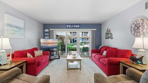 Un salon avec des canapés rouges, une table basse, un téléviseur et une pancarte sur laquelle est écrit « BIENVENUE ».
