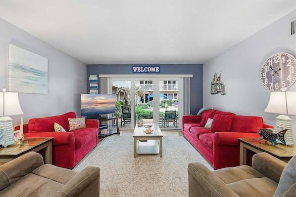 A living room with red sofas, a coffee table, a TV, and a 'WELCOME' sign.