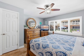 A bedroom with a bed, dresser, TV, and a window with a view.