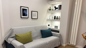 A modern living room with a grey sofa, two cushions, a white shelf with decorative items, and a radiator. - Masonber Style & Comfort in the Center of Rome: (Roma)