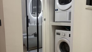 A laundry room with two stacked washing machines, a glass door leading to a shower area, and a white wall. - Masonber Style & Comfort in the Center of Rome: (Roma)