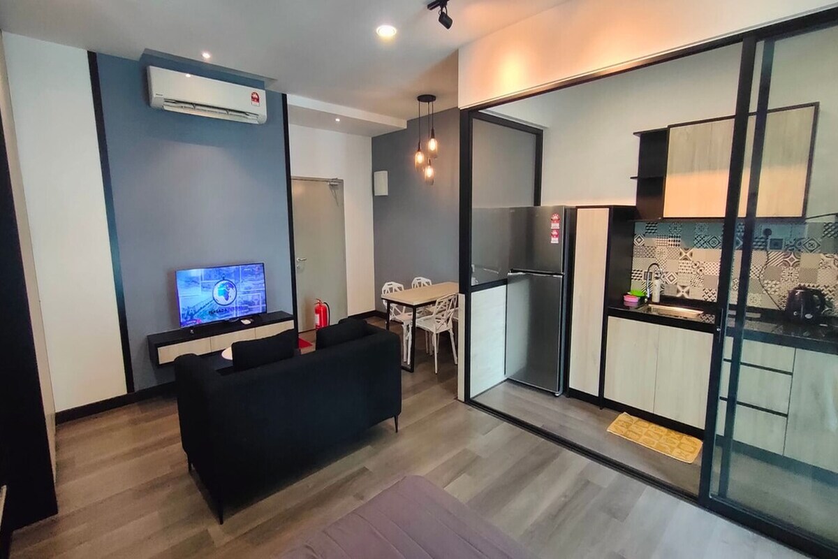 A modern living room with a flat-screen TV, a black sofa, and a dining area with a table and chairs.