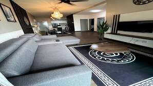 A modern living room with a sectional sofa, a flat-screen TV, and a ceiling fan. - Vista Bangi Serviced Apartments by The River (Kajang)