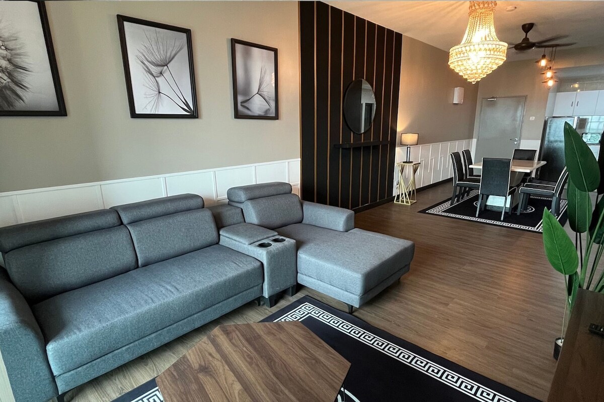 A modern living room with a grey sectional sofa, a small coffee table, and a dining area with a chandelier.